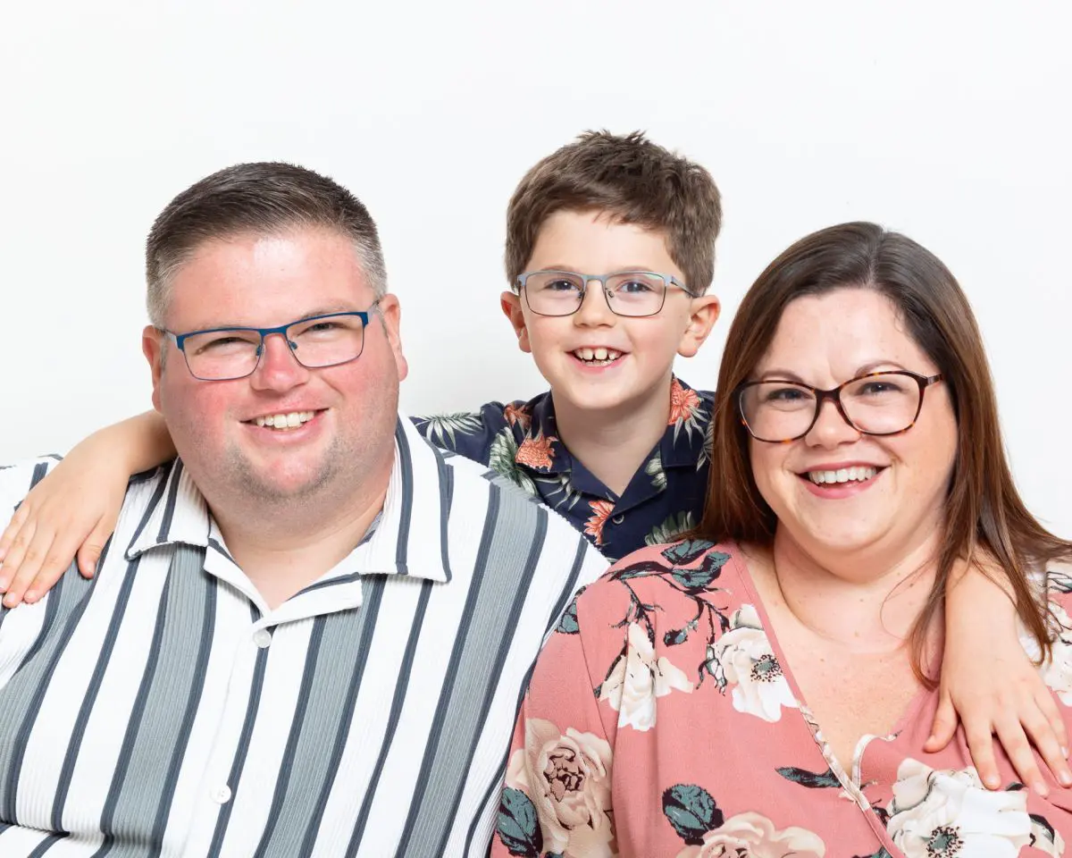 A family of mum, dad and son pose for the camera in a studio against a white background