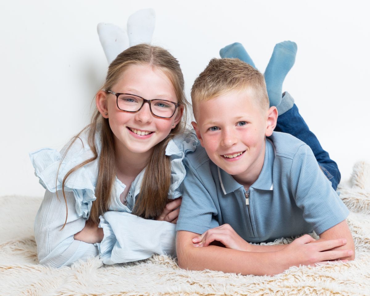 a brother and sister pose together a photo shoot lying on their tummies