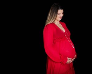 A woman poses in a red maternity dress against a black background