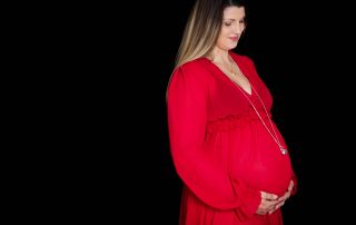 A woman poses in a red maternity dress against a black background