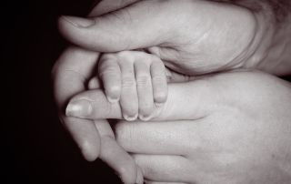 A black and white image of a parents hand holding their newborn's fingers