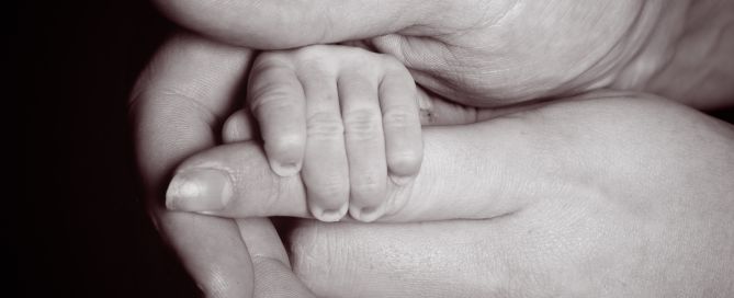 A black and white image of a parents hand holding their newborn's fingers