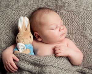 a baby lies on a grey blanket with a peter rabbit toy