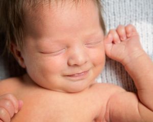 a close up of a newborn boy smiling in his sleep at a professional photo shoot