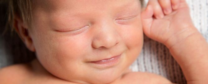 a close up of a newborn boy smiling in his sleep at a professional photo shoot