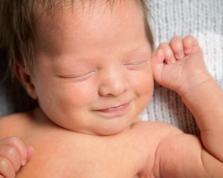 a close up of a newborn boy smiling in his sleep at a professional photo shoot