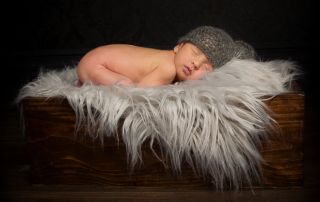 a newborn sleeps on a fluffy blanket on a wooden crate
