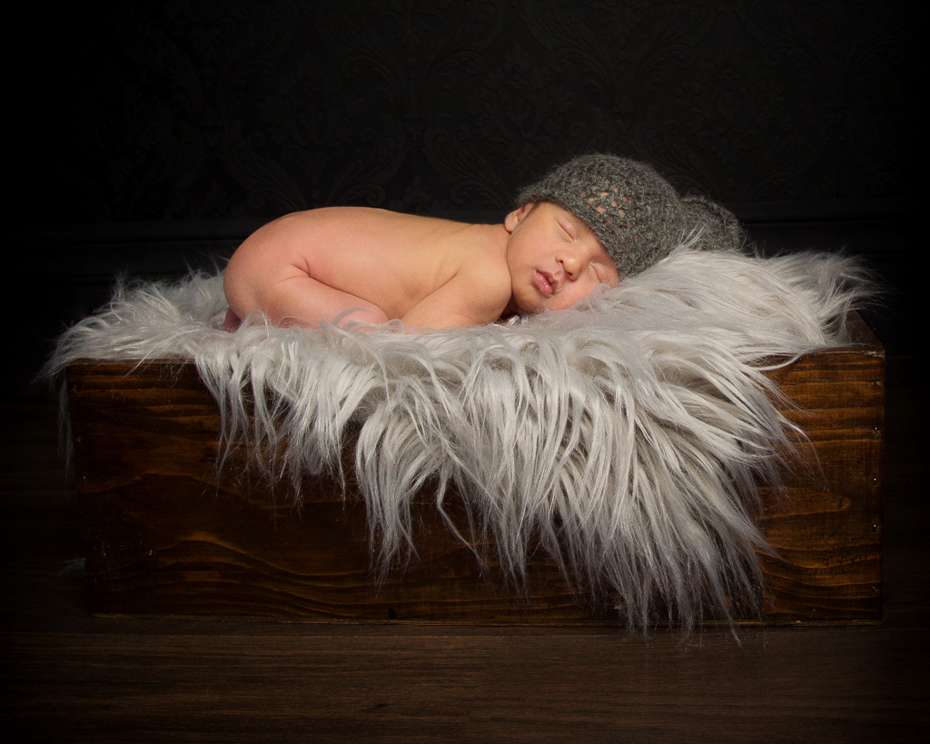 a newborn sleeps on a fluffy blanket on a wooden crate