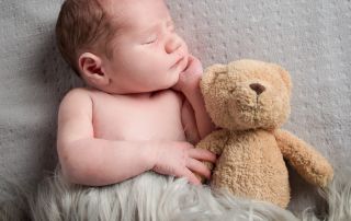 a newborn snuggles up with an old fashioned teddy bear