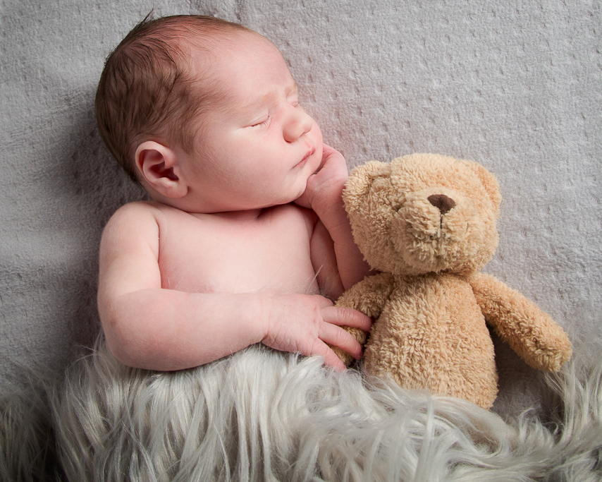 a newborn snuggles up with an old fashioned teddy bear