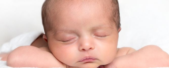 A newborn sleeps on a white blanket with their head on their hands
