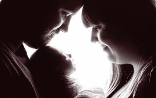 a silhouette in black and white of a couple looking down at their newborn baby