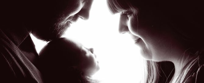 a silhouette in black and white of a couple looking down at their newborn baby