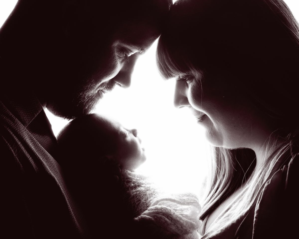 a silhouette in black and white of a couple looking down at their newborn baby