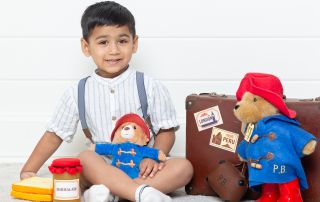 a little boy with toy Paddington bears and some themed accessories at a photo shoot