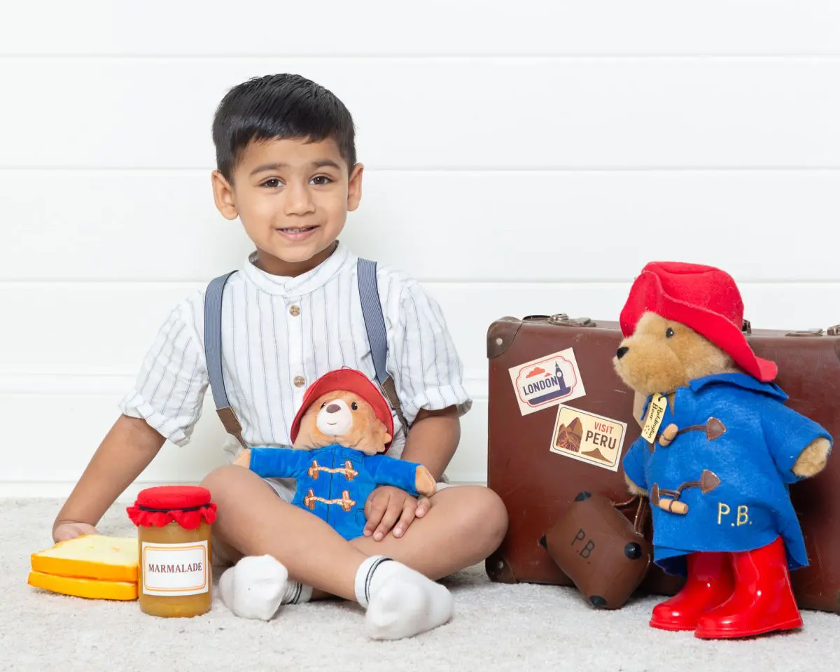 a little boy with toy Paddington bears and some themed accessories at a photo shoot