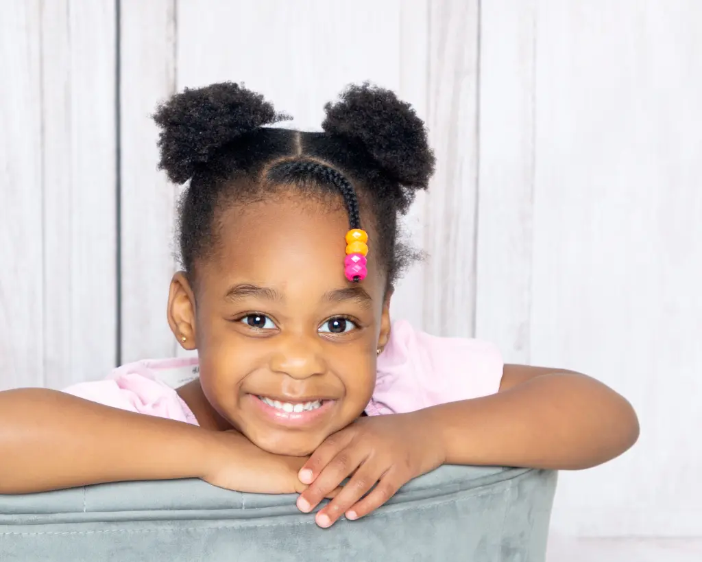A little girl smiling while posing on the back of a grey chair