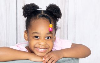 A little girl smiling while posing on the back of a grey chair