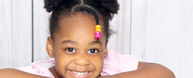 A little girl smiling while posing on the back of a grey chair