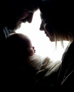 Two parents look down at their newborn in silhouette