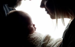 Two parents look down at their newborn in silhouette