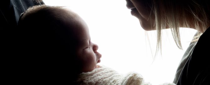 Two parents look down at their newborn in silhouette