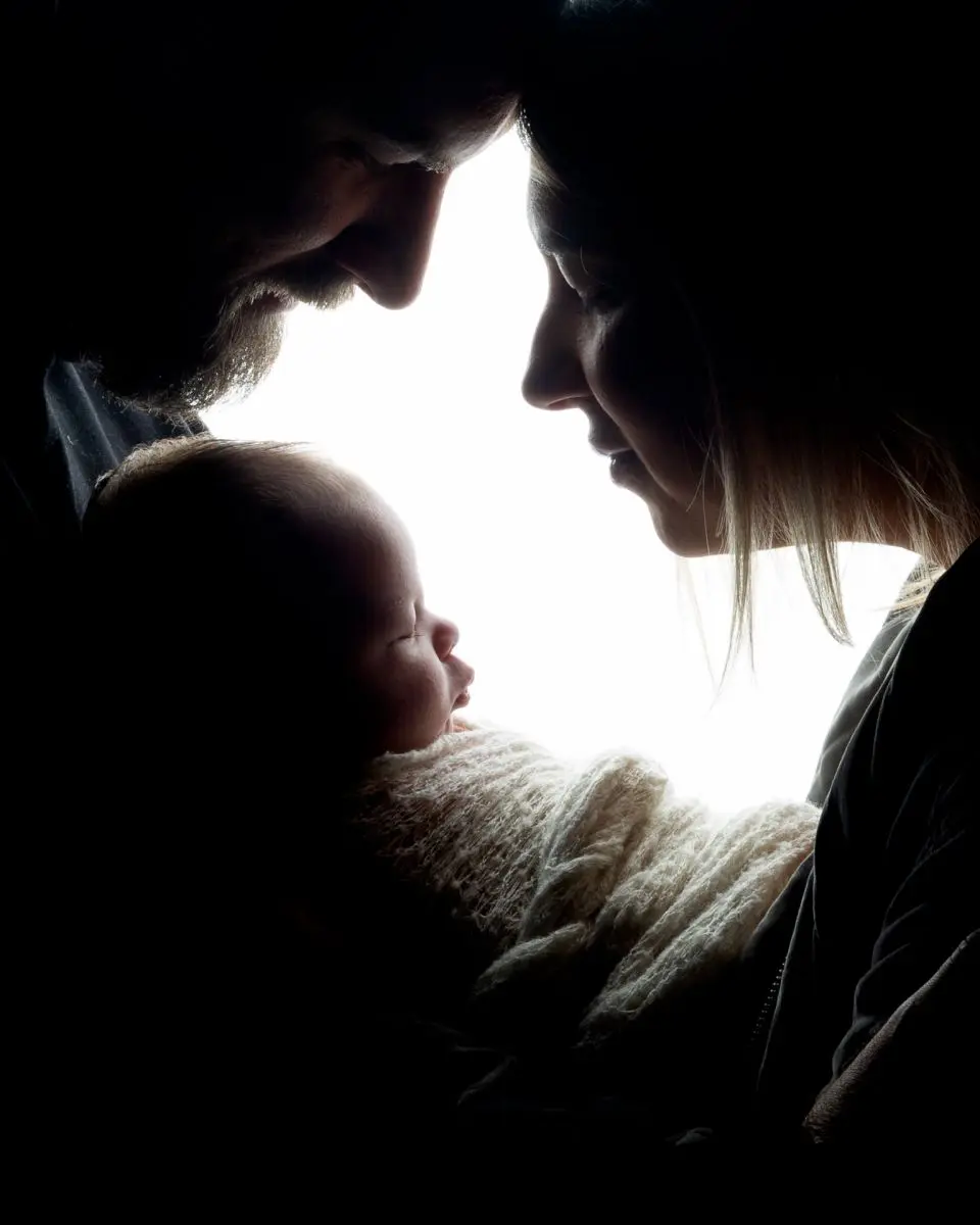 Two parents look down at their newborn in silhouette