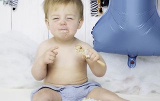 A little boy screws up his face in delight at his cake at a photo shoot
