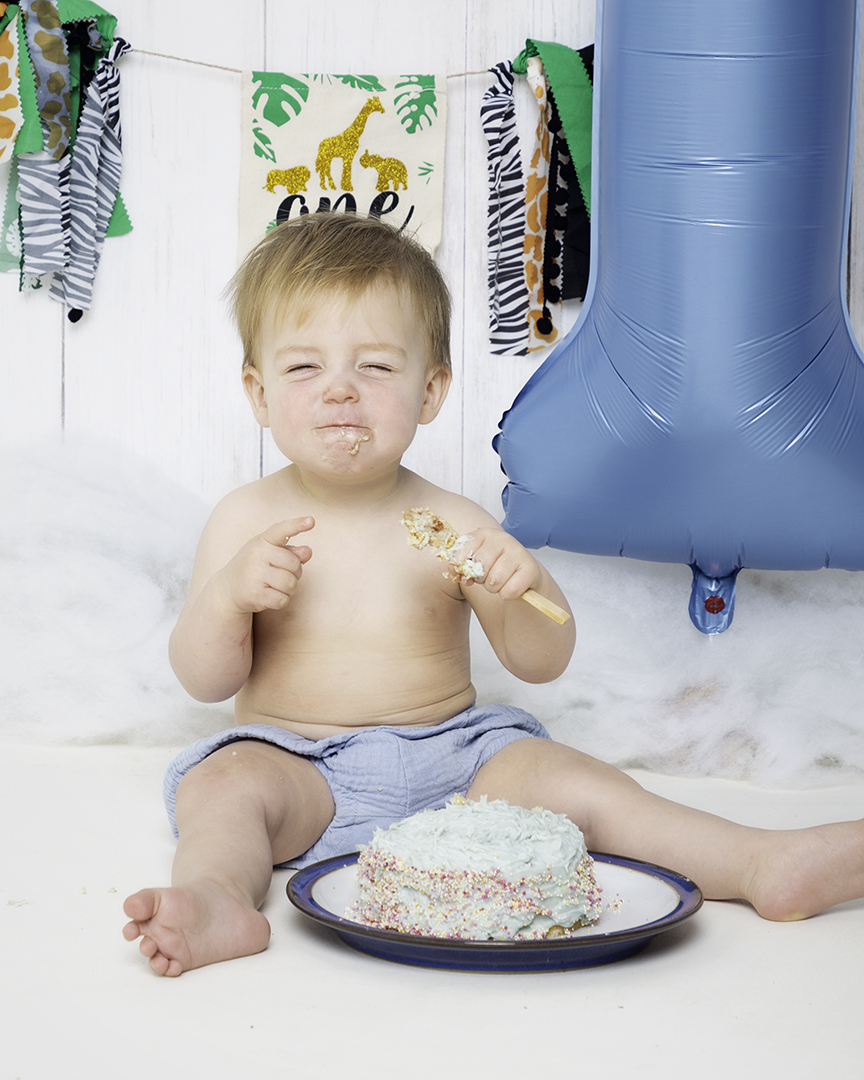 A little boy screws up his face in delight at his cake at a photo shoot