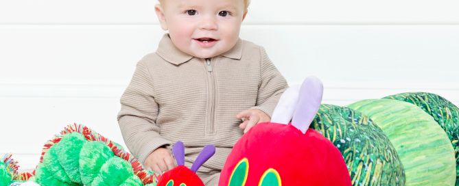 A baby sits with two hungry caterpillar toys