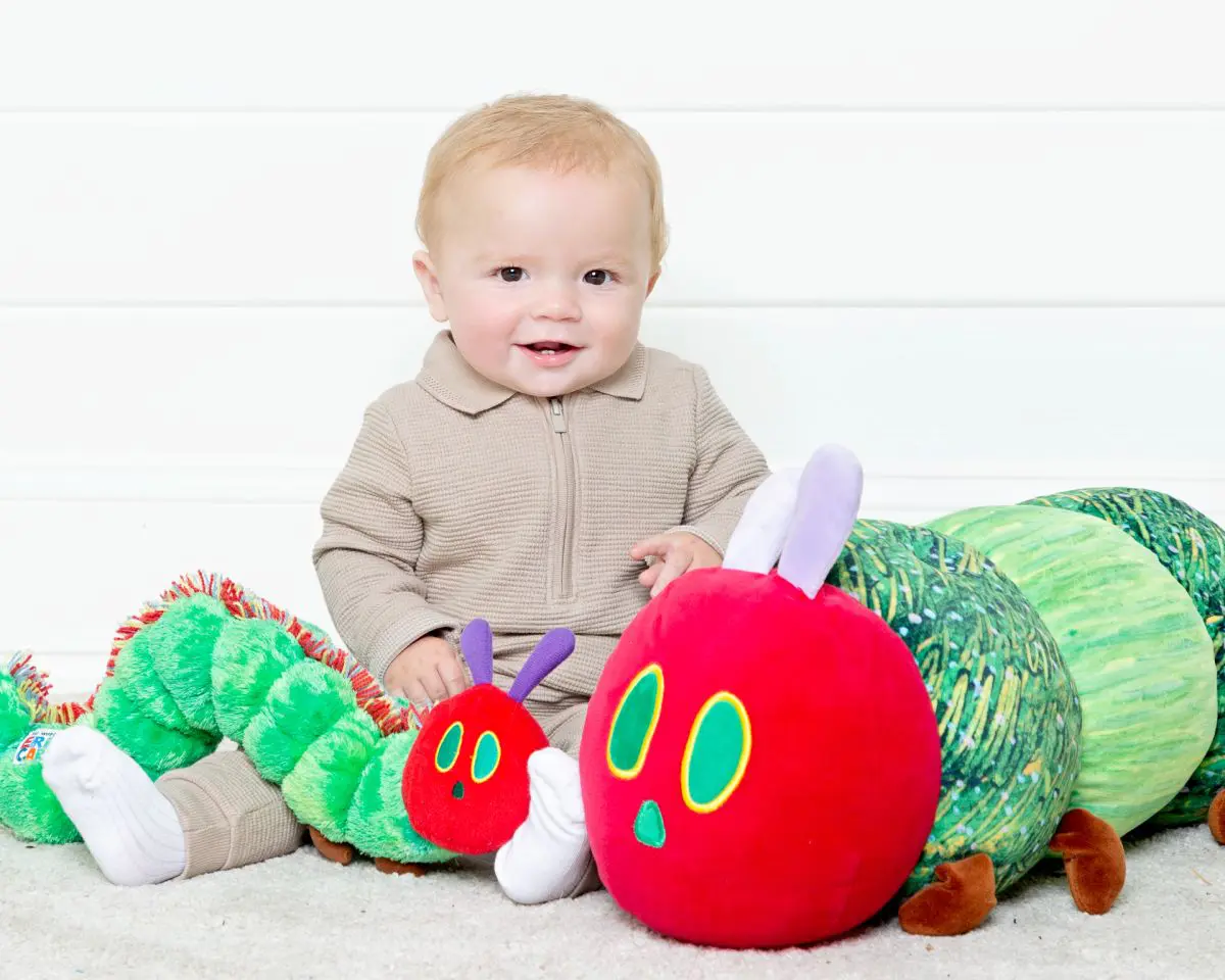 A baby sits with two hungry caterpillar toys