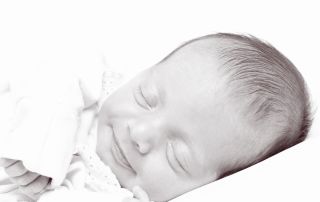 A black and white image of a smiling newborn sleeping on their side
