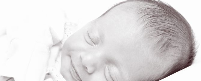 A black and white image of a smiling newborn sleeping on their side