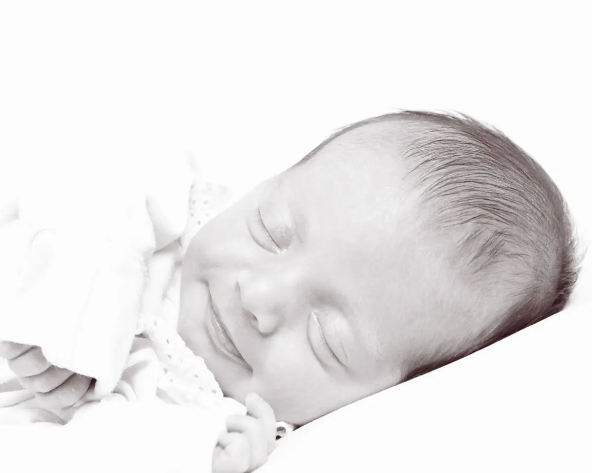 A black and white image of a smiling newborn sleeping on their side