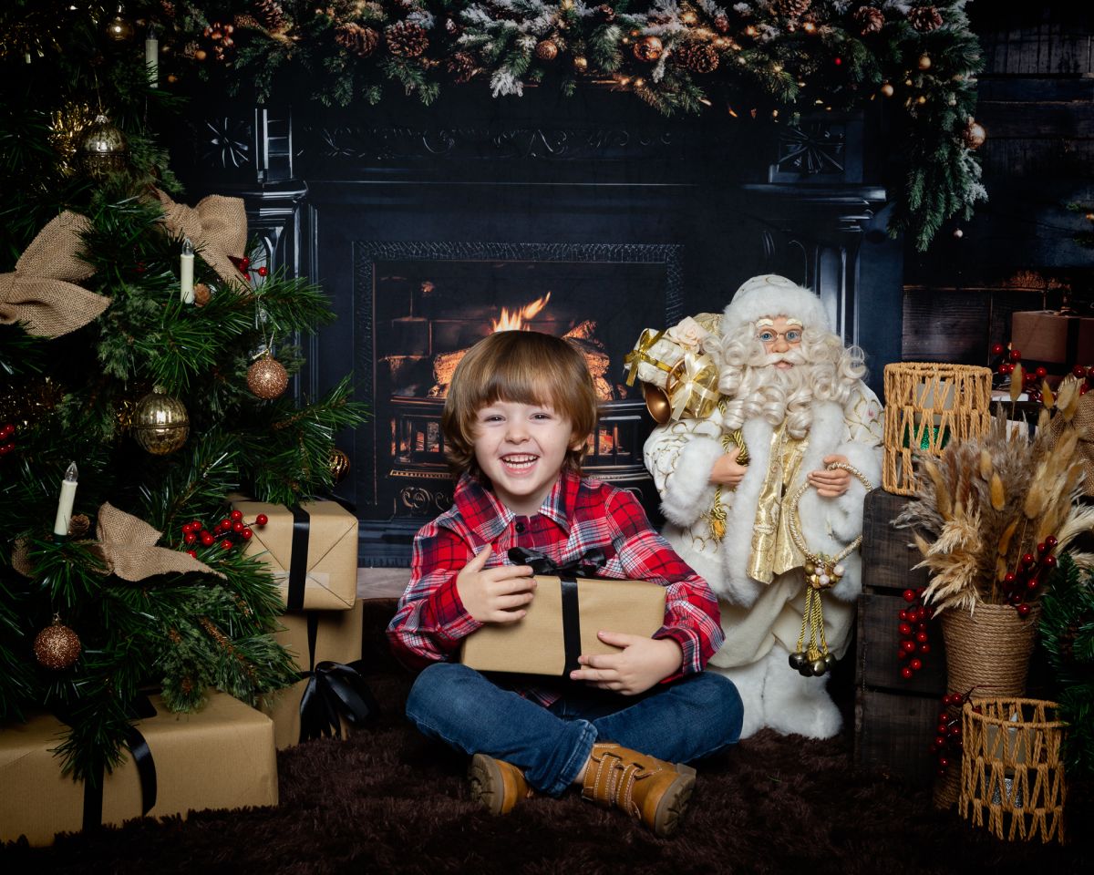 Christmas Photo Shoots West Sussex 2025 a little boy poses with a present in a Fireside themed Christmas set