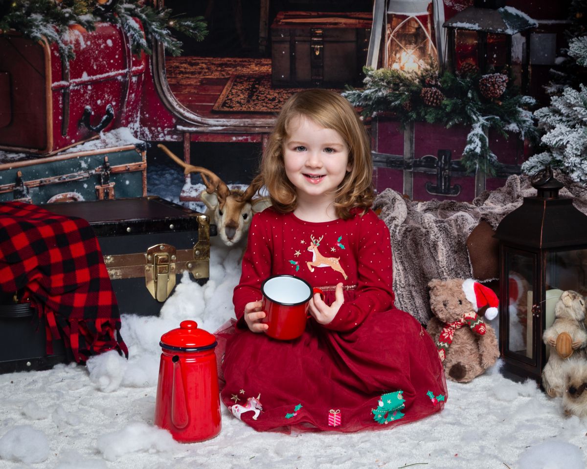 Christmas Photo Shoots West Sussex 2025 a little girl in a red dress poses in a Christmas themed set