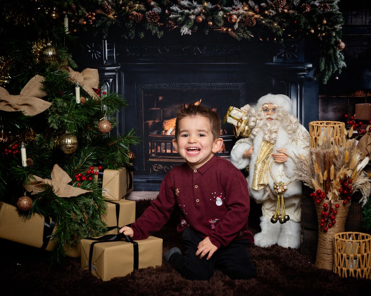 Christmas Photo Shoots West Sussex 2025 a boy in a burgundy shirt poses in a Fireside themed Christmas set