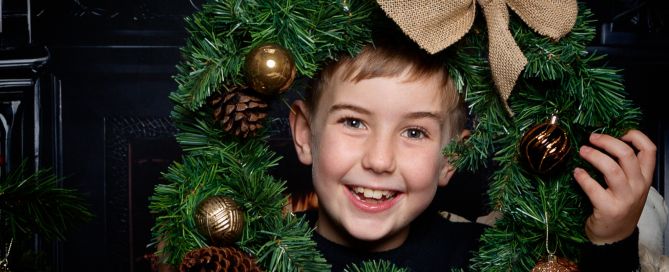 a boy smiles through a wreath in a Fireside themed Christmas set