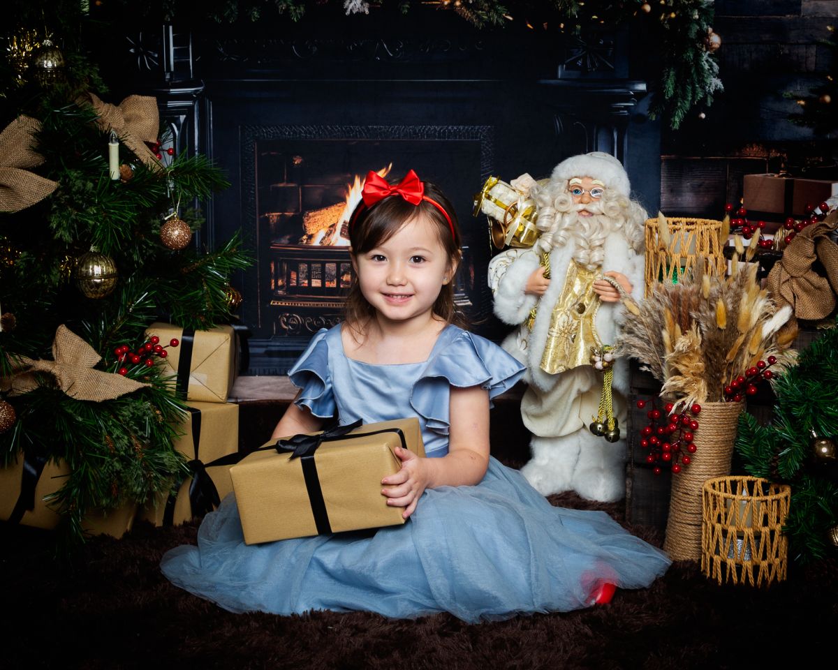 Christmas Photo Shoots West Sussex 2025 a little girl in a blue dress poses in a Fireside themed Christmas set
