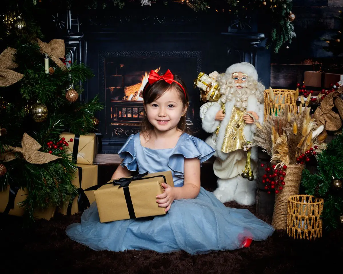 a little girl in a blue dress poses in a Fireside themed Christmas set