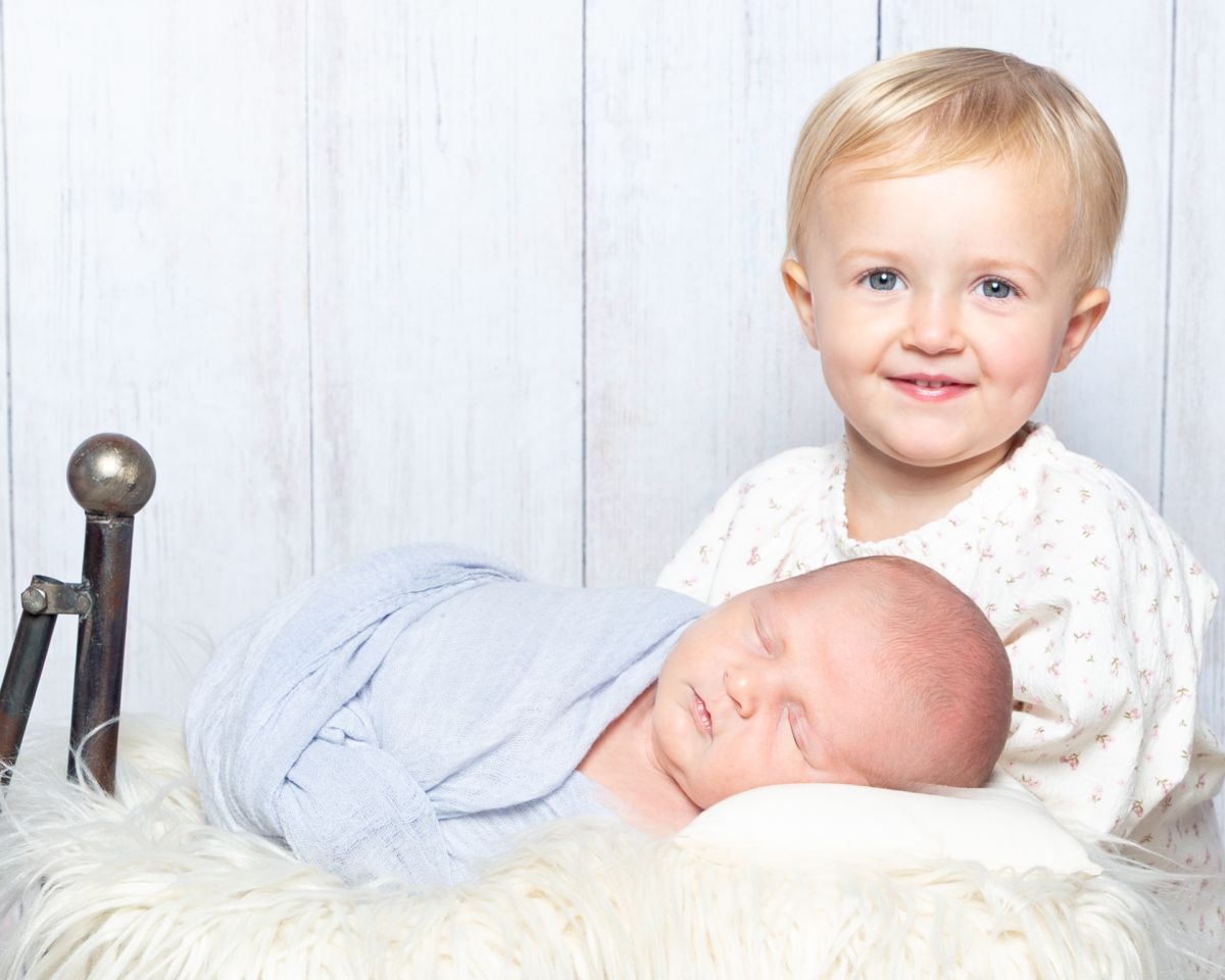 a proud big sister poses beside her sleeping newborn brother