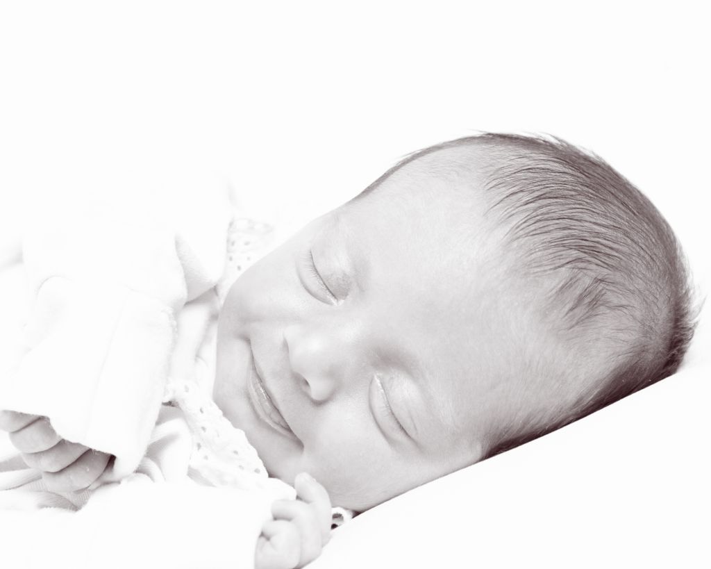 a black and white image of a softly smiling newborn