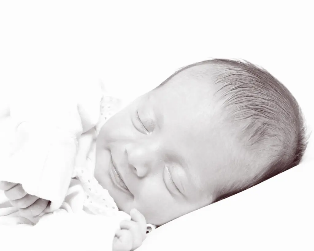 a black and white image of a softly smiling newborn