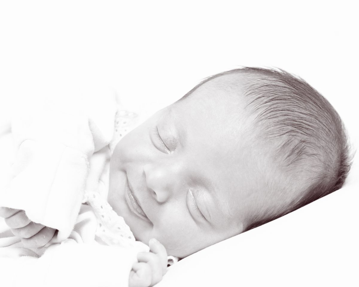 a black and white image of a softly smiling newborn