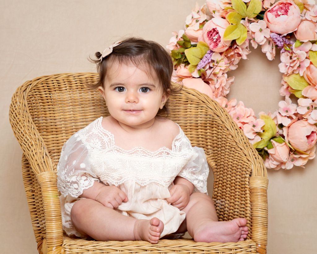 a baby in a lace dress in a wicker chair