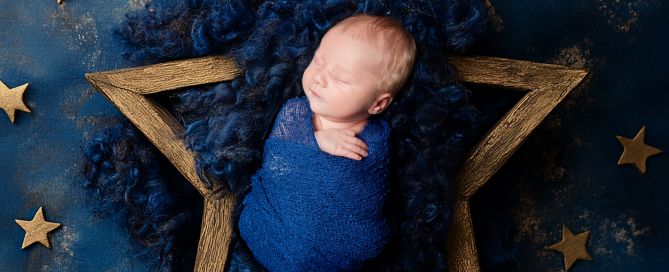 A sleeping newborn wrapped in a blue swaddle posed in a star shaped bowl