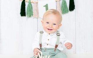 a little boy in a green outfit at his first birthday cake smash shoot
