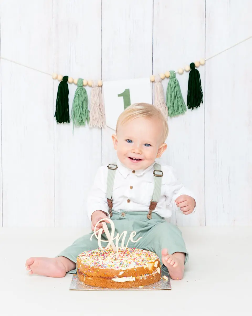 a little boy in a green outfit at his first birthday cake smash shoot