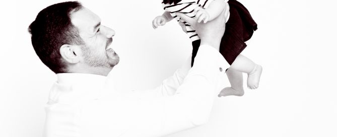 A black and white image of a dad playing with his infant daughter