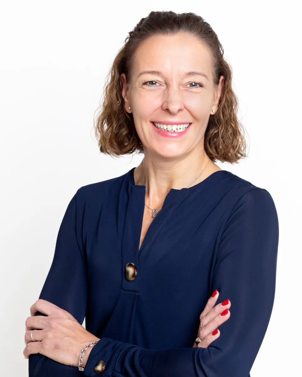 A business headshot of a woman with folded arms and a blue top